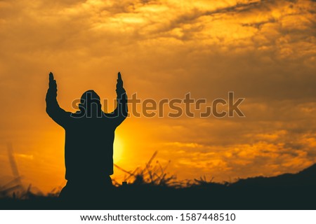 Man kneeling down and raise two hands to sky for praying to God at sunset background. christian silhouette concept.