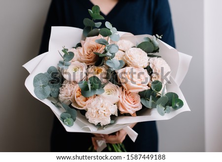 Very nice young woman holding big and beautiful bouquet of fresh roses, carnations, eucalyptus flowers in pastel pink colors, cropped photo, bouquet close up Royalty-Free Stock Photo #1587449188