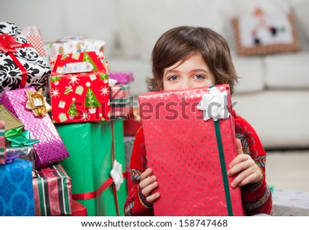 Portrait of boy holding Christmas gift in front of face at home