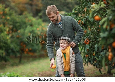 A child a boy and a man in warm sweaters smile and look at the camera on the street in a garden with trees.