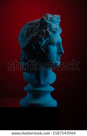 Plaster statue of a bust of Apollo Belvedere in blue local light on a red background