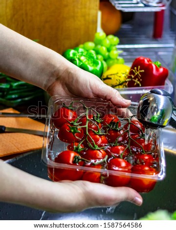 Preparation of fresh salad with tomatoes. Fresh vegetables on the worktop near to sink in a modern kitchen interior, healthy food concept. Selective focus.A bunch of tomatoes is rinsed under a sink.