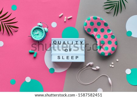 Healthy night sleep creative concept. Sleeping mask, alarm clock, earphones, earplugs and pills. Split two tone, pink and grey paper background with circles and palm leaves. Sweet dreams!