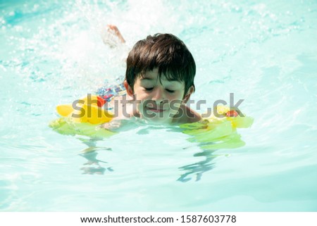 Boy in pool with yellow float playing in water making faces and stamping feet in water