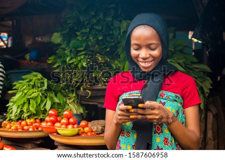 young african woman selling in a local market smiling while using her mobile phone Royalty-Free Stock Photo #1587606958