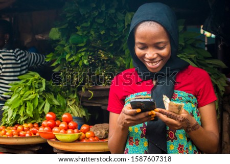 young african woman selling in a local market smiling while using her mobile phone Royalty-Free Stock Photo #1587607318