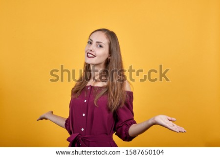 Young woman confused and doesn't know what to do, but teen laughs. Lady are pointing hands in diffirent directions She is dressed up in burgundy bluse. Behind her there is isolated orange wall