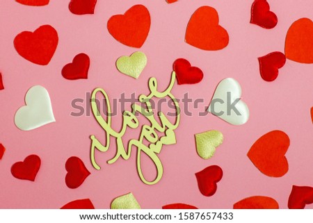Valentine's Day background flat lay. On a pink background red paper hearts, hearts made of white fabric and red satin and the inscription made of wooden letters, I love you.