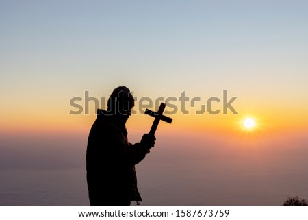 Silhouette human praying and holding christian cross for worshipping God at sunset or sunrise background.Christian, Christianity, Religion copy space background. 