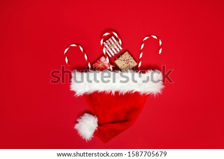 2020 New year template. Stylish decor concept, christmas small gift boxes, candy cane, Santa Claus hat on red backdrop. Flat lay, copy space. Background for postcard, for greetings