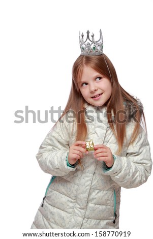 Studio image of a cute cheerful little girl in a warm white coat with a crown on his head holding a small gift isolated on white
