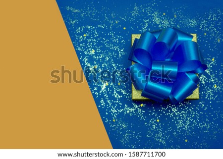 Gift with a large blue bow on a blue background with sequins. Orange background for your text. Festive concept.