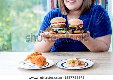 Asian fat women Happy to eating with the food she prepared Which has fried chicken, hamburger and pizza, This picture focuses on hamburger, to Cholesterol and excess fat concept.