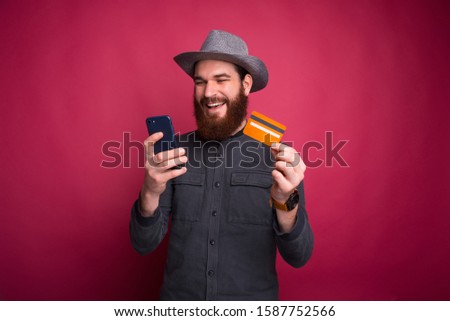 Young happy man with beard making online shopping and holding credit card and smartphone