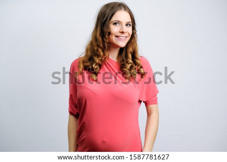 Portrait of beautiful pregnant young woman. Girl with wavy hairs smiling on grey background. Happy pregnancy