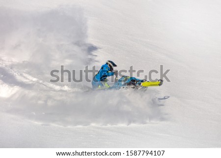 Pro snowmobiler makes a turn and lets a flurry of snow spray from under the caterpillar. sports snowmobile in the mountains. radial turn of the snowmobile on a steep slope. Winter fun moto extreme