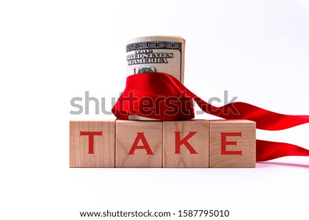 Four wooden cubes with the word "TAKE" and a roll of dollars and a red ribbon