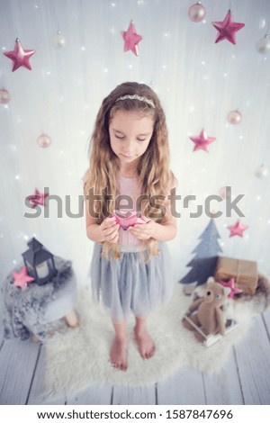 Young sweet girl with beautiful dress on christmas background with fairy lights and pink stars