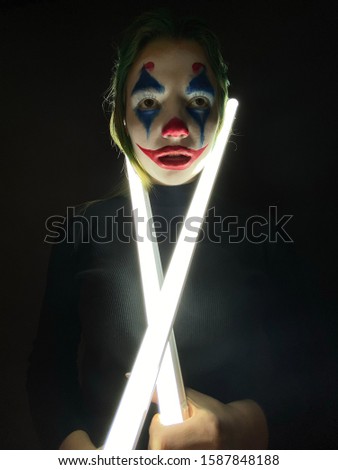 Portrait of a girl with clown makeup holds a glowing lamp on a black background.