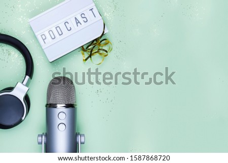 Top view photo of podcast concept - lightbox with letters podcast on it, headphones and professional microphone on the table