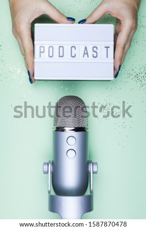 Womans hands holding sign podcast on lightbox and professional mic on the table. Top view shot of podcast studio premier on mint background with gold glitter
