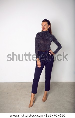 business woman in blue pants and jacket stands in the Studio against a blue wall