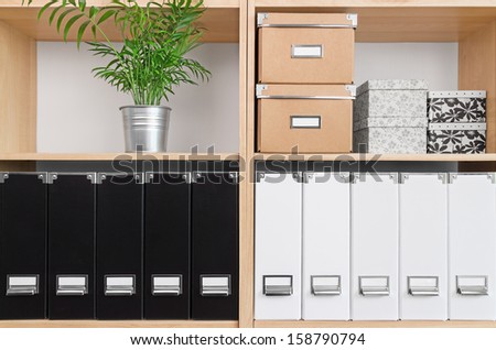 Shelves with storage boxes, black and white folders, and green plant. Royalty-Free Stock Photo #158790794