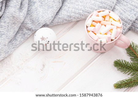 Cup of hot chocolate with marshmallows near gray knitted fabric on a white wooden background (planks). Christmas concept. Top view. Copy space.