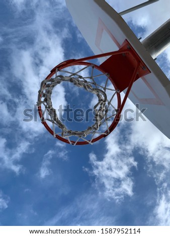 Looking up through a basketball hoop with blue sky and clouds
