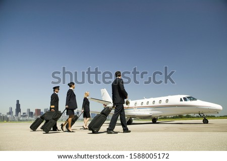 Flight crew wheeling suitcases to airplane on tarmac Royalty-Free Stock Photo #1588005172