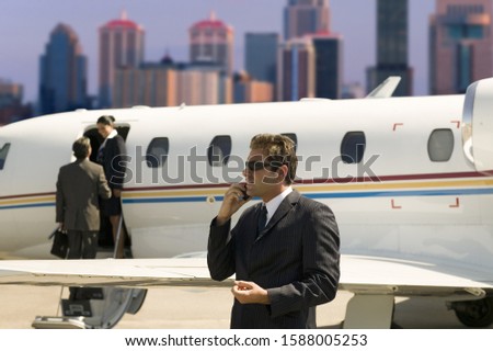 Businessman using cell phone next to airplane on tarmac
