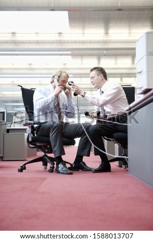 Two businessmen using telephones from opposite cubicles