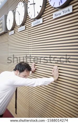 Businessman leaning on wall under world time zone clocks