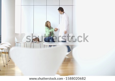 Male doctor shaking hands with woman in waiting room