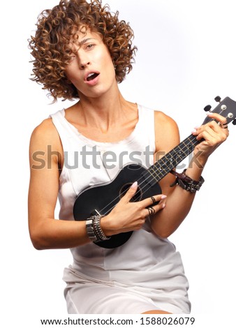 Young attractive woman with curly hair in a white dress plays on the ukulele