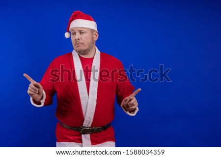 Emotional male actor in costume and hat of Santa Claus posing on a blue background.
