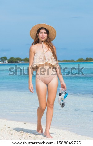Young woman with wet skin and with a snorkel standing on sand and going to swim in clear sea