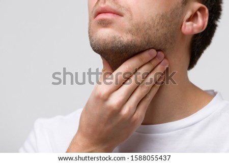 Close up of sick man suffering from throat problems, grey background, isolated. Thyroid gland, painful swallowing, pharyngitis, laryngeal swelling concept. Inflammation of the upper respiratory tract Royalty-Free Stock Photo #1588055437