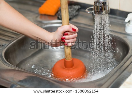 woman cleans plunger with clogged sink, close up Royalty-Free Stock Photo #1588062154