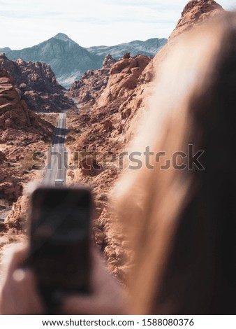 Close up of a girl taking a picture of the view of the rocky mountains with a road that crosses in the Valley of Fire. Nevada State United States of America.