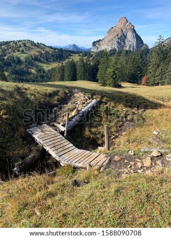 Picture of a little bridge on a train with somemountains in the background. The Picture was taken in the Alps.