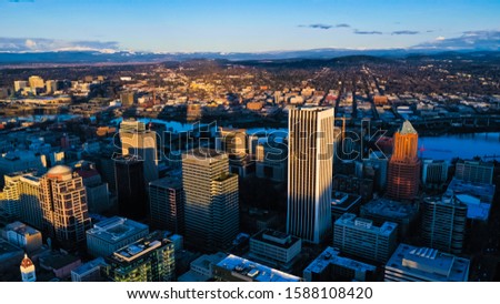 An aerial depiction of Portland, OR's financial district is dramatically lit by the setting sun. 