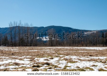 Panoramic view of field covered with snow patches and blue sky in the background