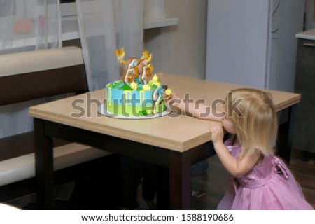girl pulls her hand to the cake standing on the table for her birthday