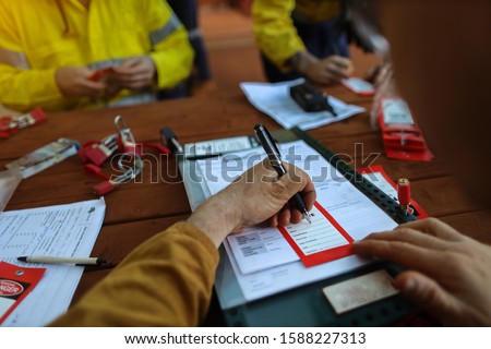 Worker writing they name on red danger tag and sign onto personnel red danger lock before placing locking into isolation permit safety control box prior start work each shift   Royalty-Free Stock Photo #1588227313