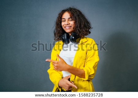 Woman showing pointing on brick wall background. Very fresh and energetic beautiful young girl smiling with headphones on neck. Closeup