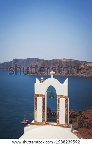 Traditional Greek white church arch with cross and bell in village Oia, Santorini Greece