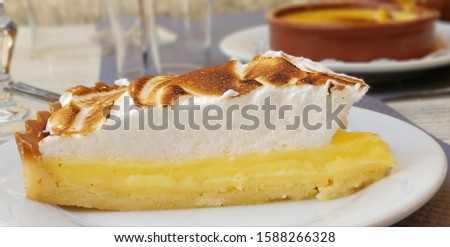 Thick Lemon meringue pie on a restaurant table with crème brûlée in the background. 