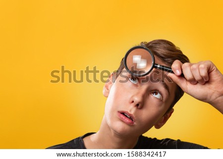 The concept of search. A close up portrait of teenager in a black t-shirt, surprised, presses a paw to his forehead and looks through it. Yellow background. Copy space.