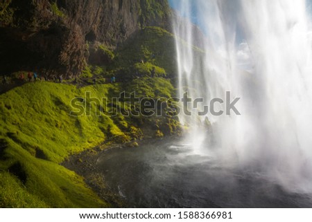 Amazing waterfall Seljalandsfoss in Iceland and tourist near it. The waterfall drops 60m (197 ft) and is part of the Seljalands River. Visitors can walk behind the falls into a small cave
